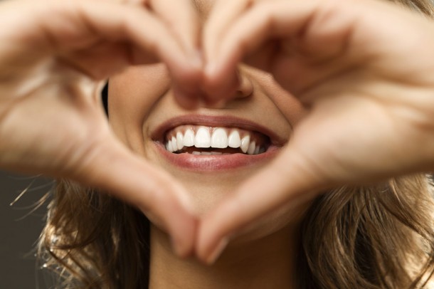 woman's smile and hands in a heart shape in front of face