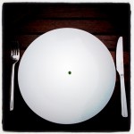 single pea in the middle of a white plate, knife and fork